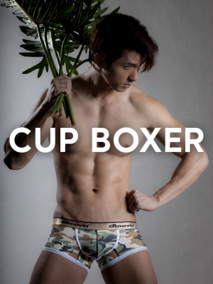 Male model wearing camouflage cup boxer underwear, posing with a plant and a gray background, with 'CUP BOXER' text across the image.